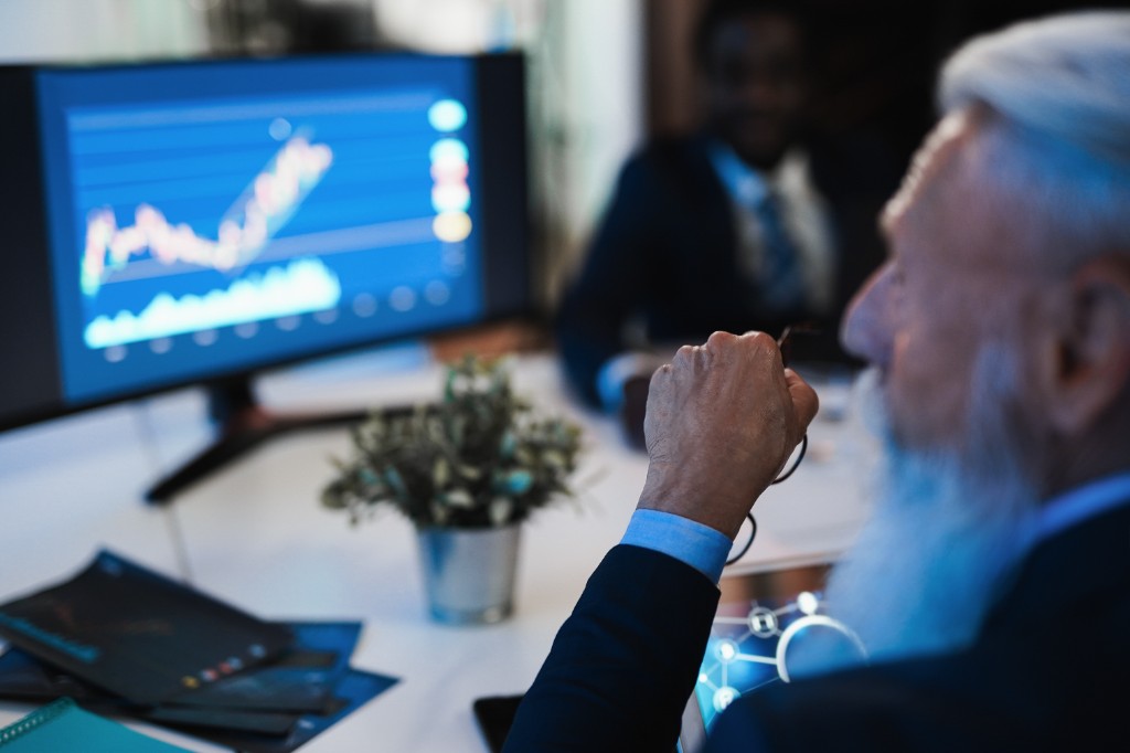 Senior professional studying financial line charts on a large monitor in a modern office