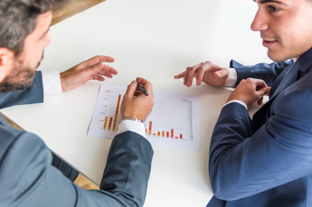 Two professionals in suits reviewing printed charts and data visualizations at a white table