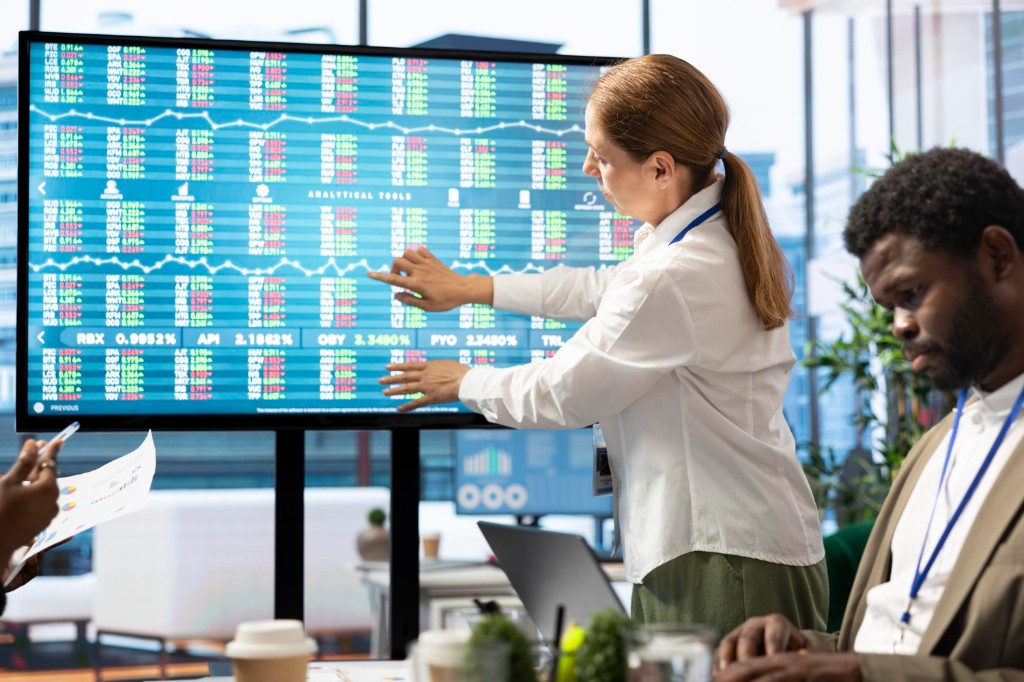 Team in a modern office reviewing charts and data as a presenter points to a large display